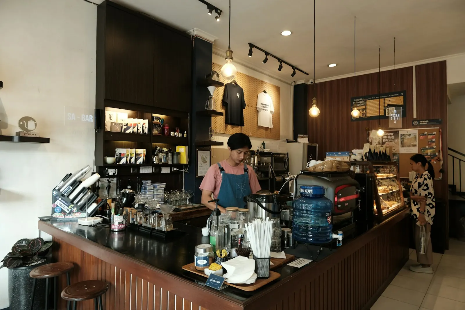 Medewerker achter de toonbank van een lunchroom, met koffiemachine en vitrine
